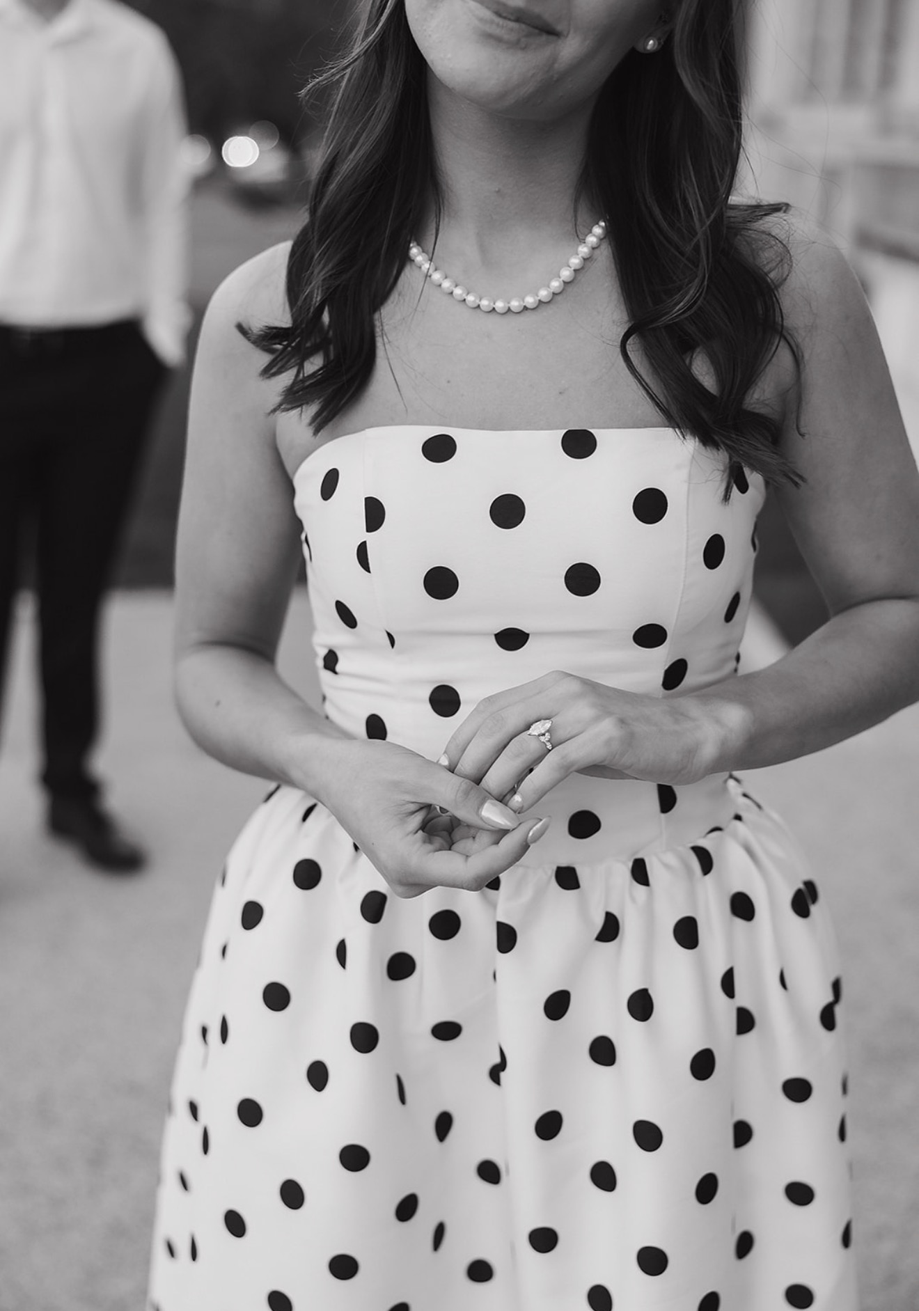 Black and white photo of a woman in a polka-dot dress showing her engagement ring