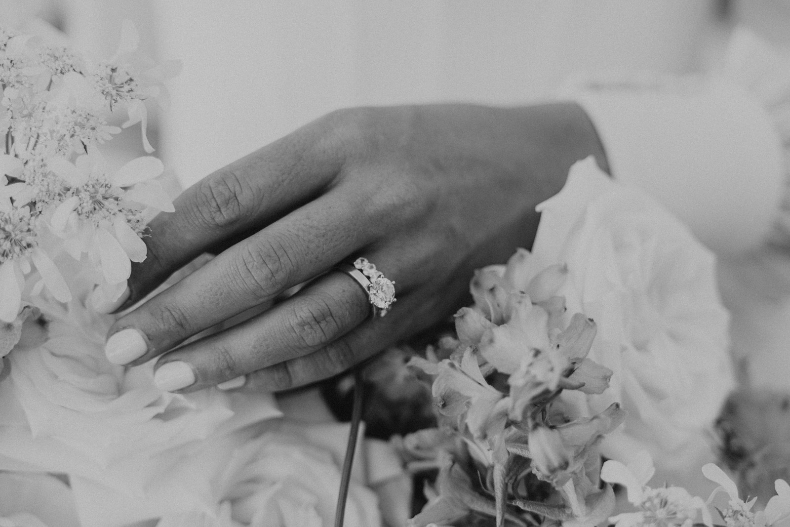 Black and white close-up of a hand wearing an engagement ring among flowers